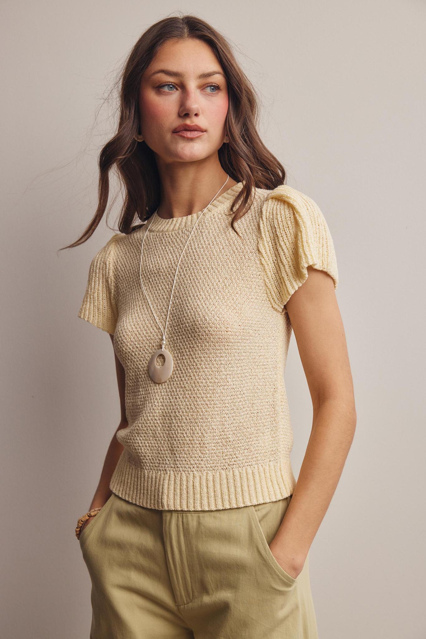 Woman wearing a beige knitted top and light green pants against a neutral background