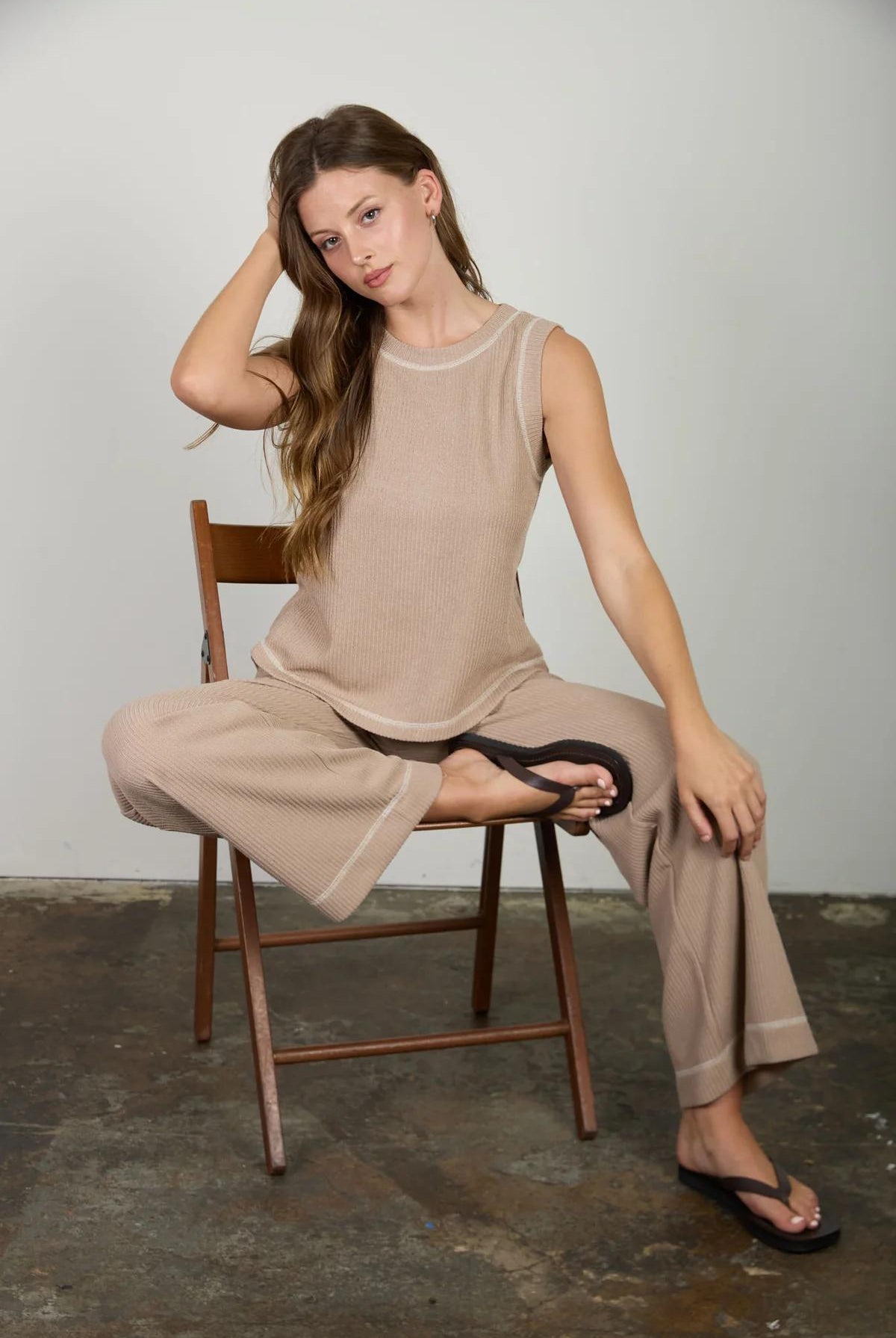 Woman sitting on a chair wearing a beige outfit against a plain background