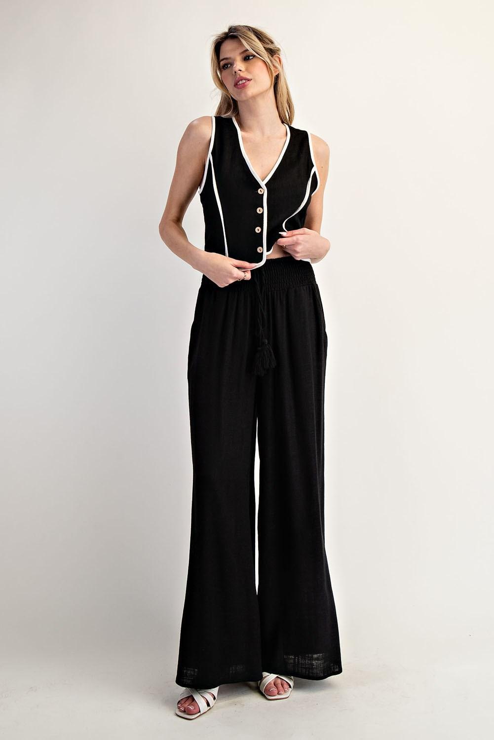 Woman wearing a black pants and black vest with white trim on a white background