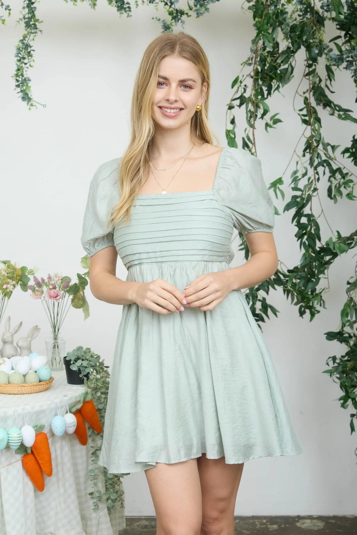 Woman in a light green dress standing in front of a decorated Easter table with flowers and carrots.