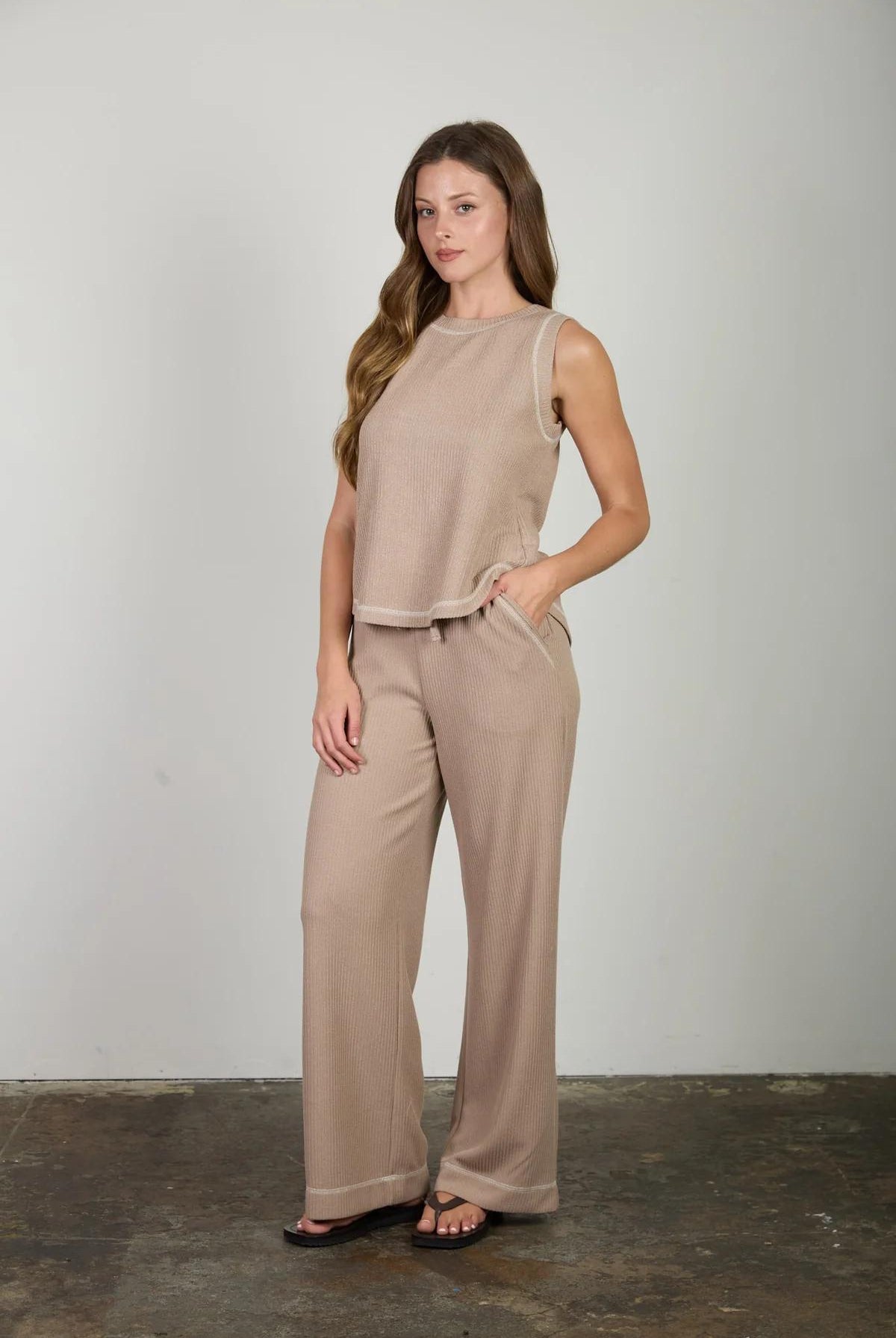 Woman wearing a beige sleeveless top and pants against a plain background