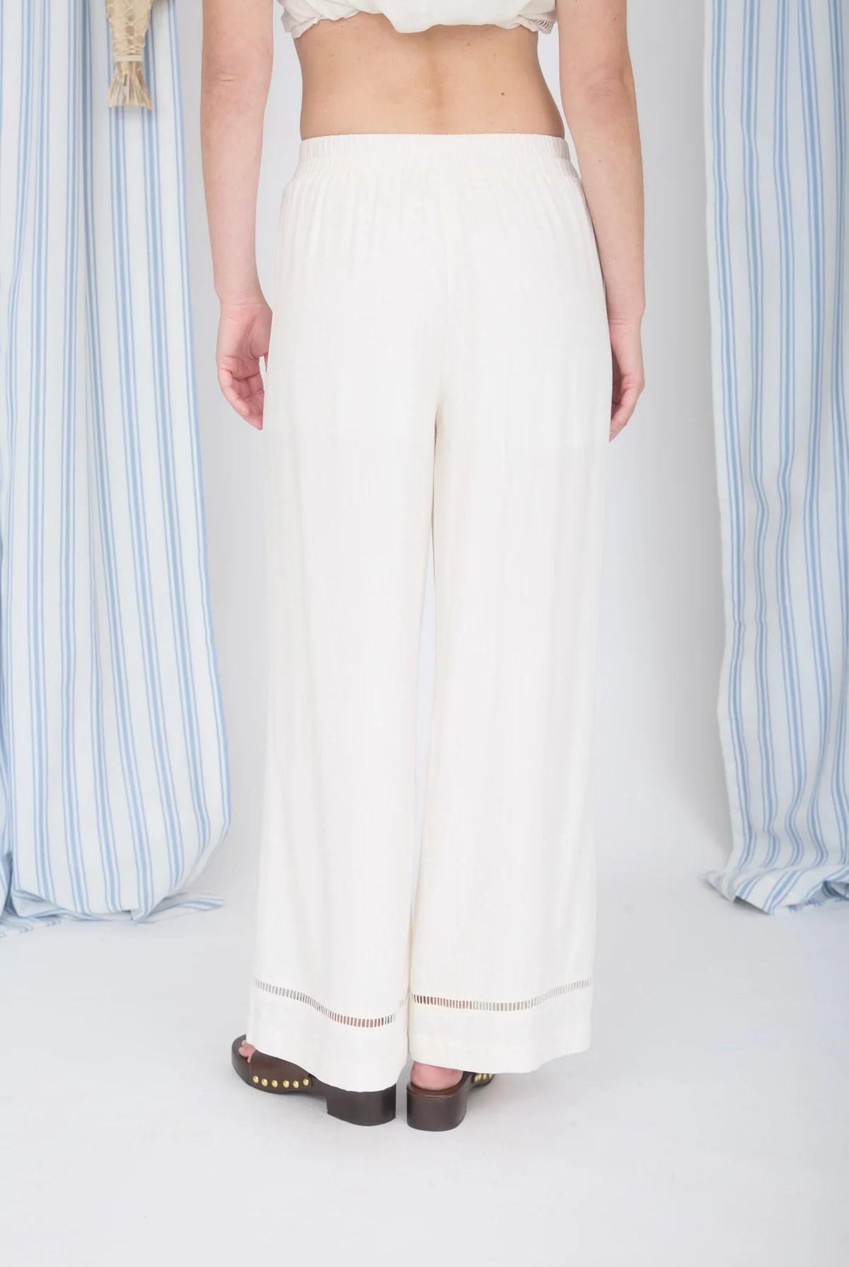 Person wearing a white outfit with wide-leg pants against a striped curtain background