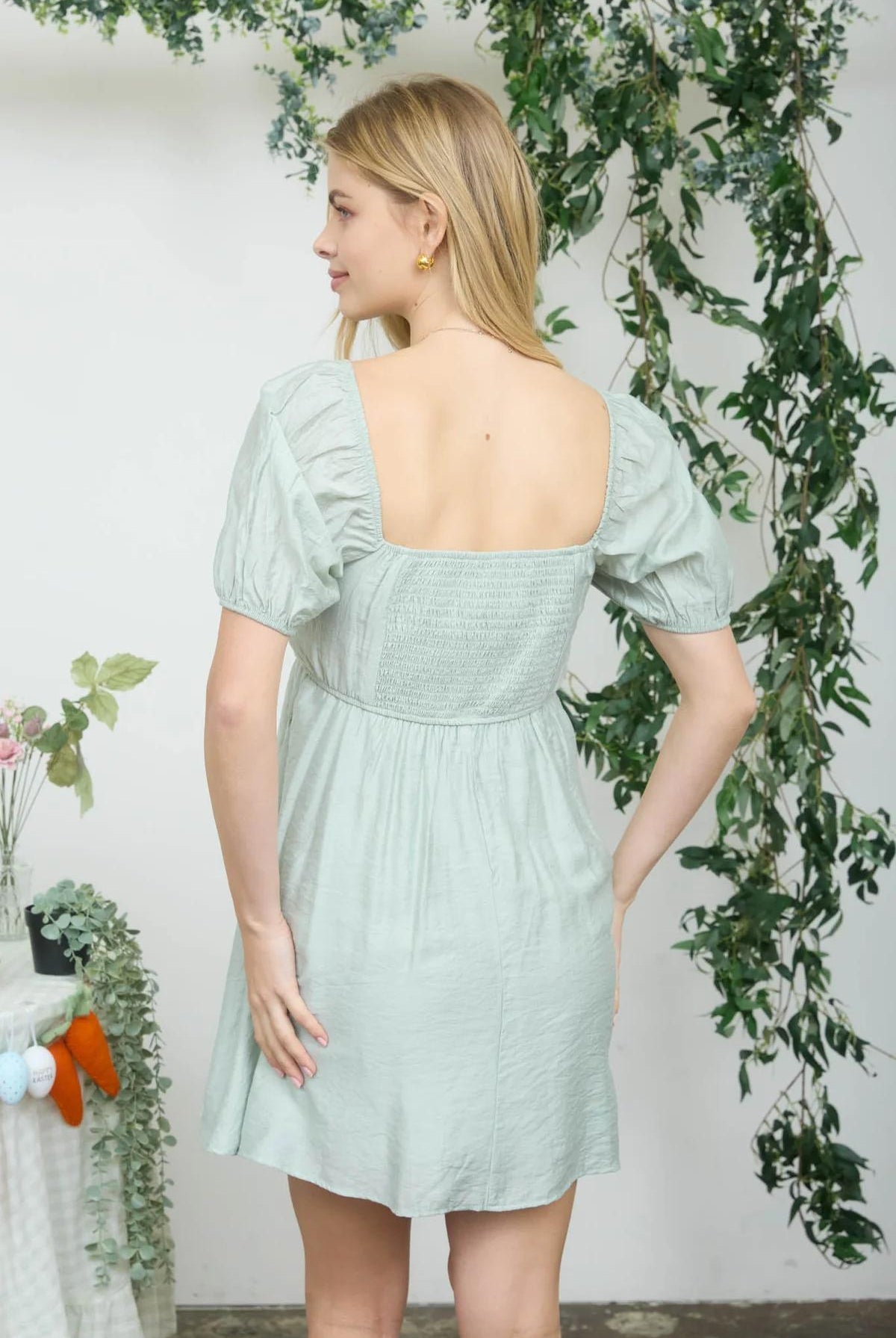 Woman wearing a light green dress with floral decorations in the background