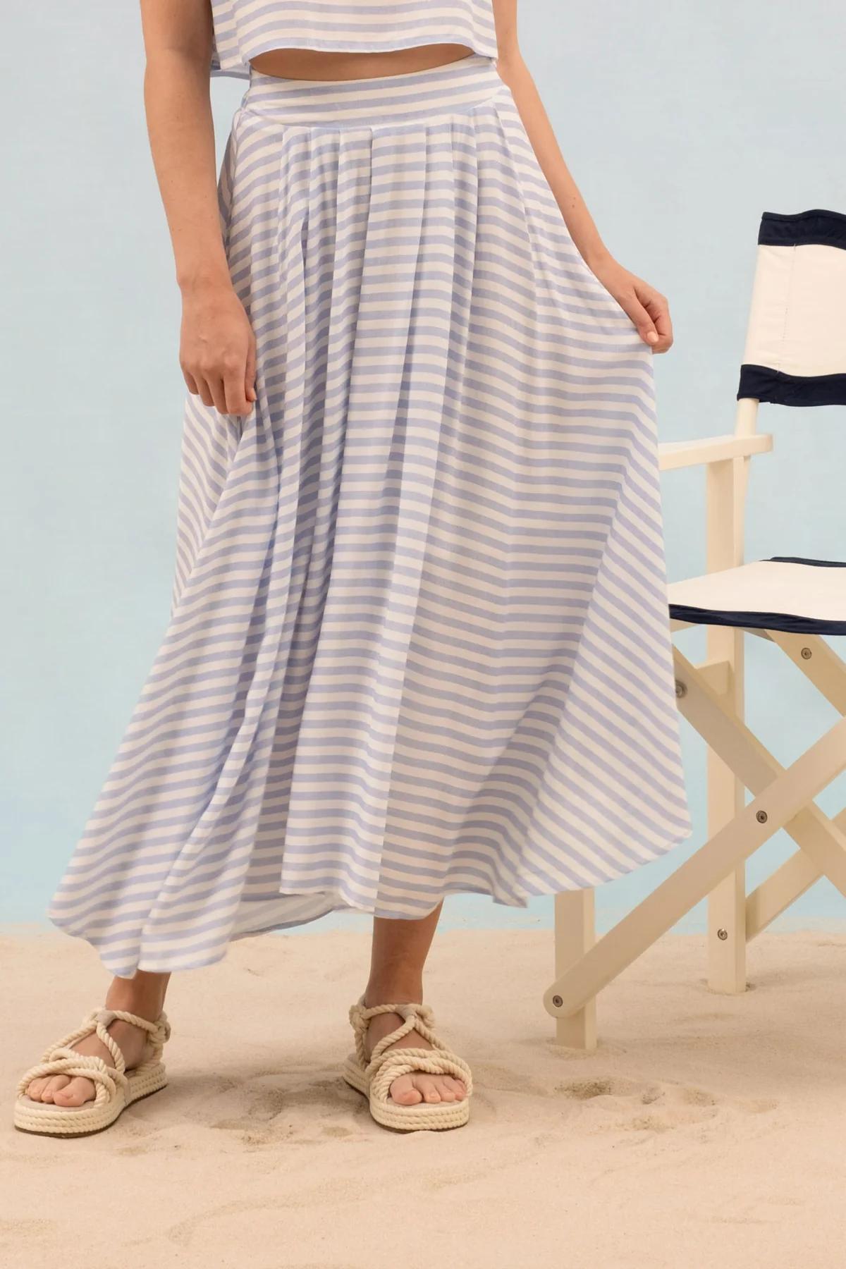 Person wearing a striped dress standing on a sandy beach with a chair in the background.