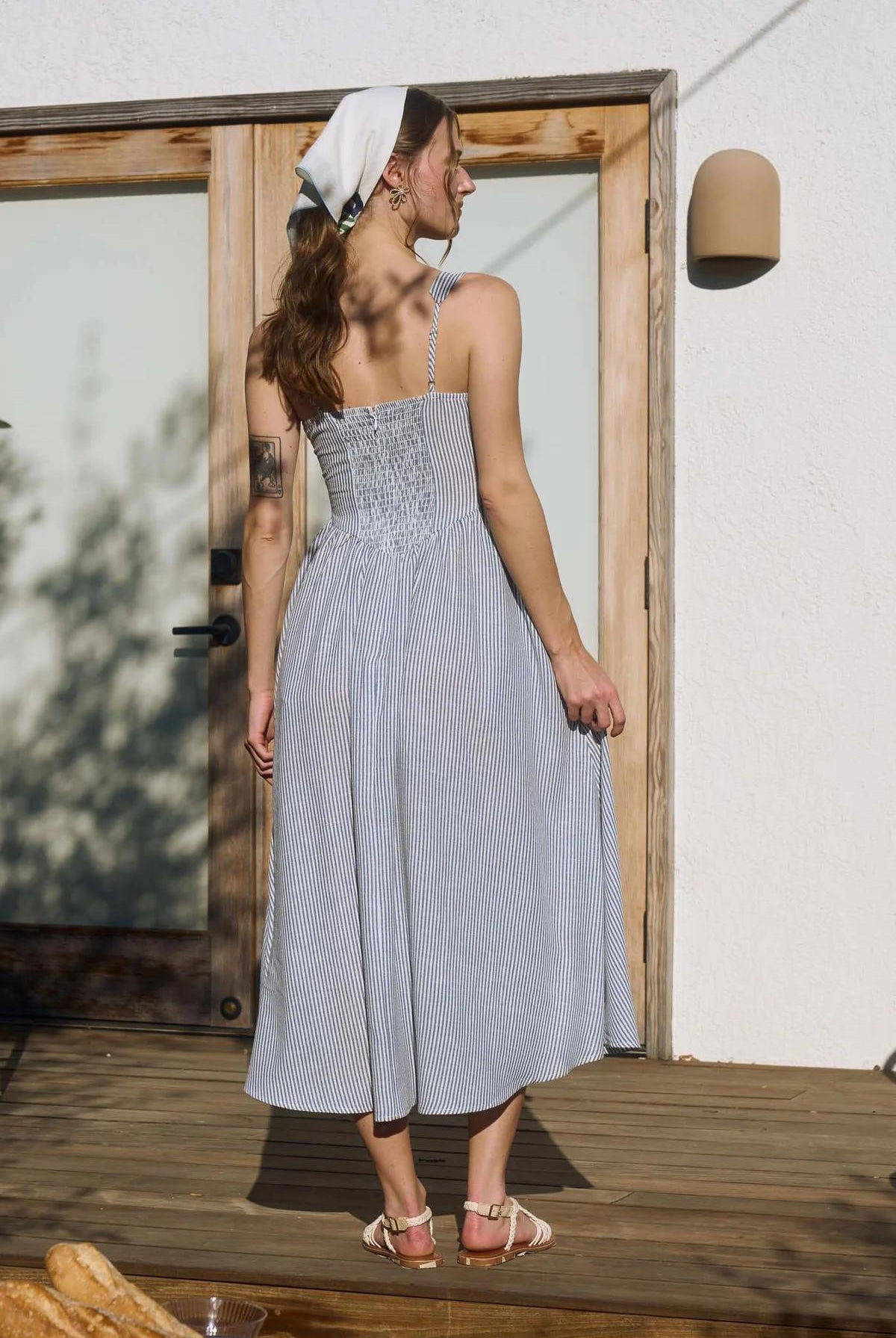 Woman in a light blue dress standing on a wooden deck.