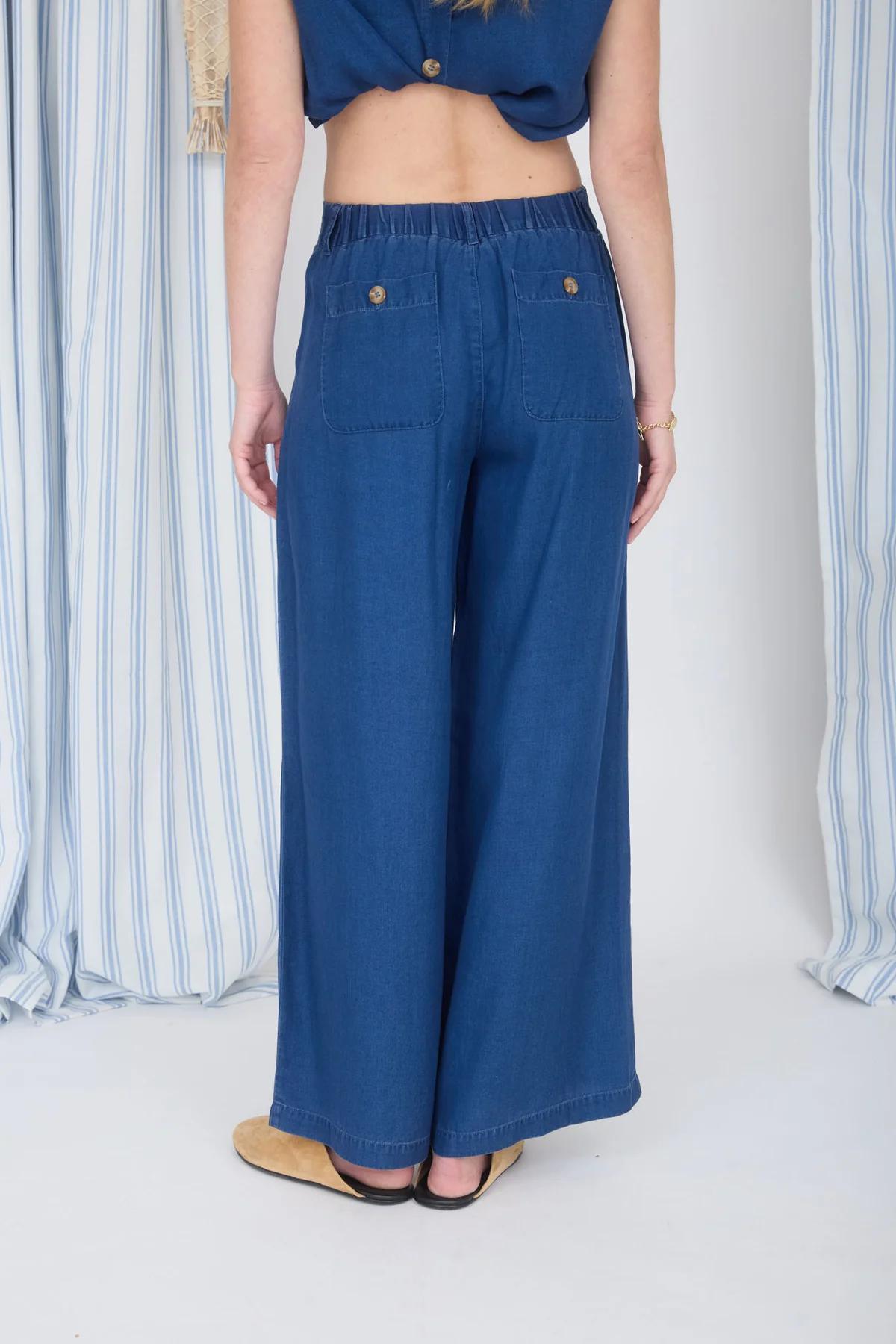 Person wearing blue wide-leg jeans standing against a white background with striped curtains.