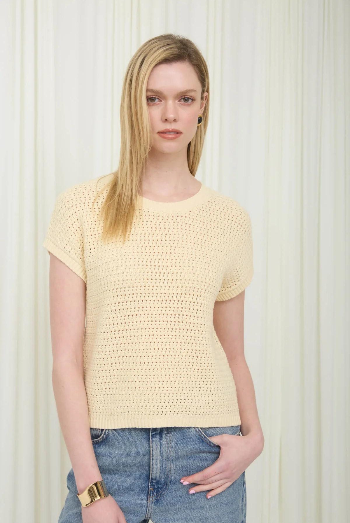 Woman wearing a yellow textured top and blue jeans against a white background