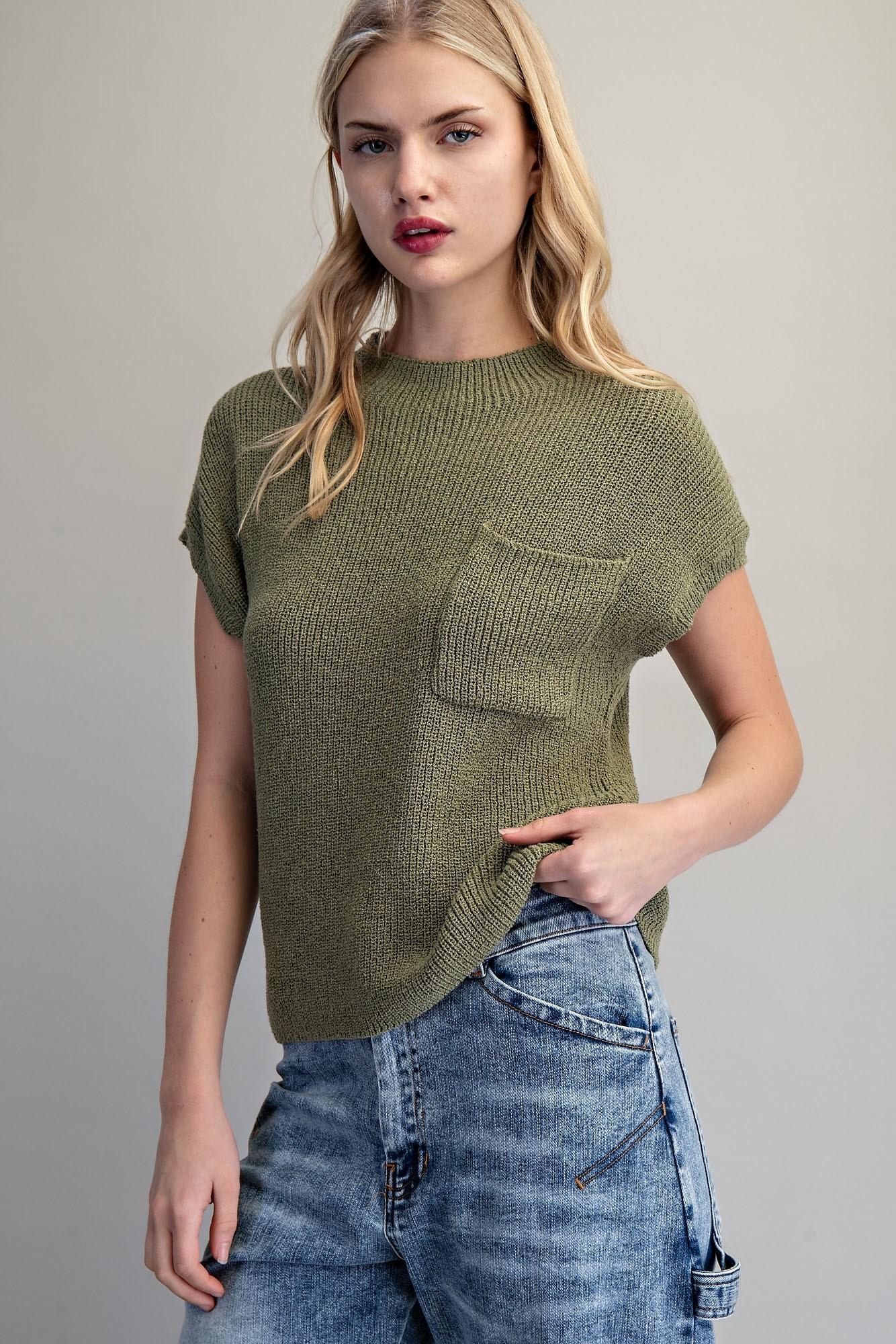 Woman wearing a green knitted top with a pocket and blue jeans on a plain background