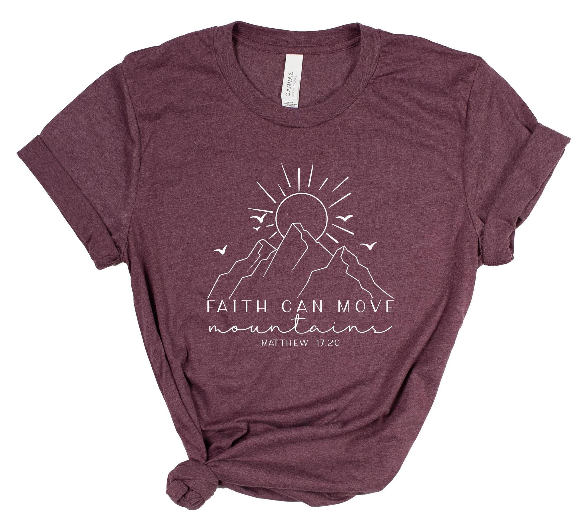 Maroon t-shirt with mountain and sun graphic and 'Faith can move mountains' text on a white background