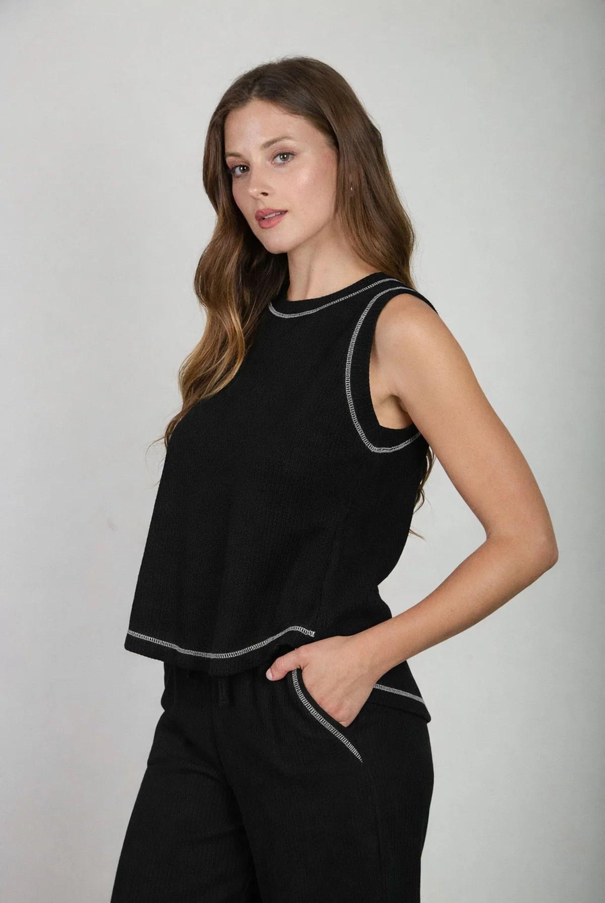Woman wearing a black sleeveless top with white trim on a plain background