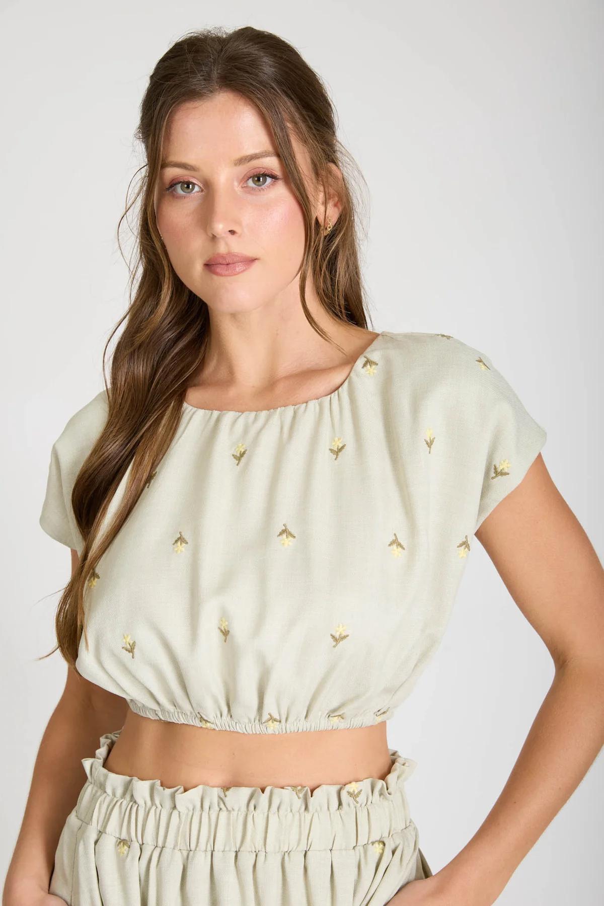 Woman wearing a light green top with small patterns on a plain background