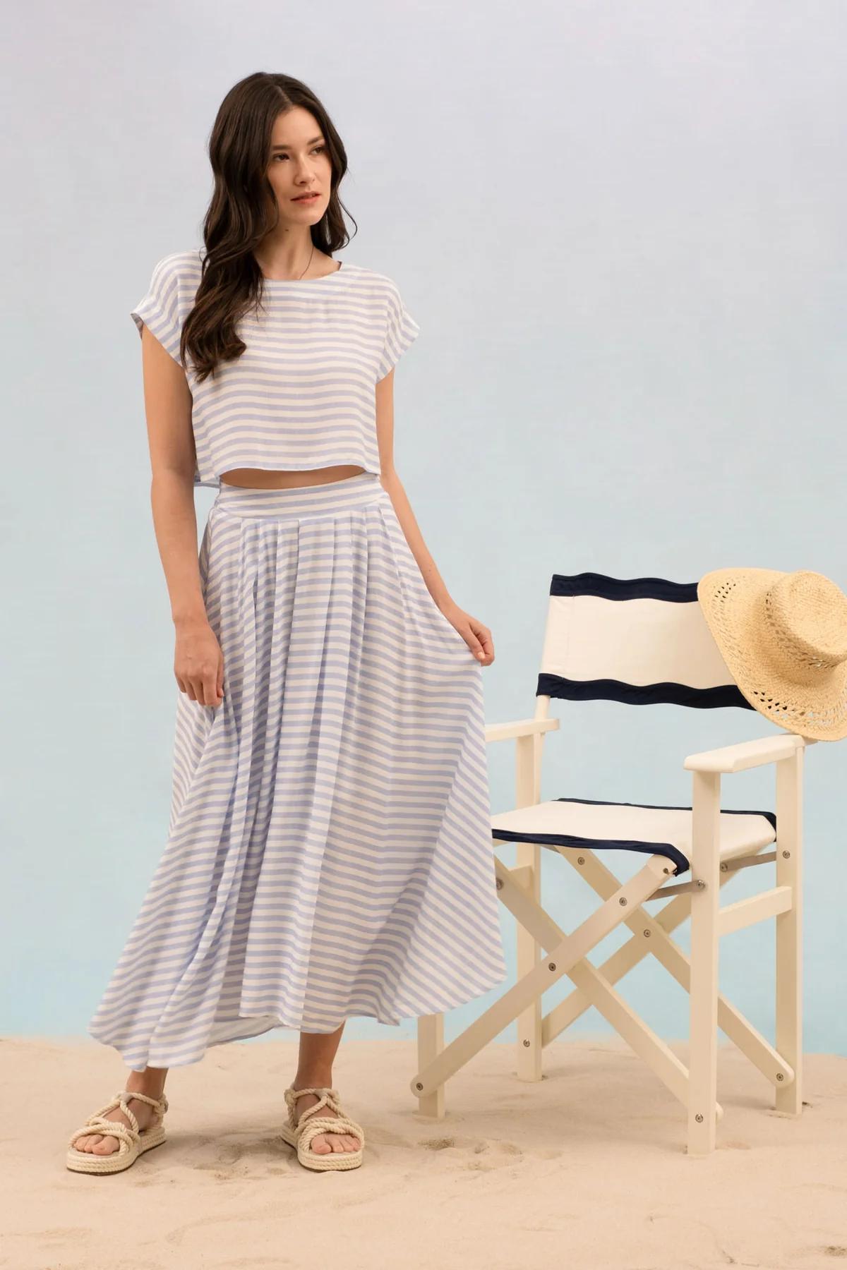 Woman in a striped outfit standing next to a director's chair with a straw hat on a light blue background
