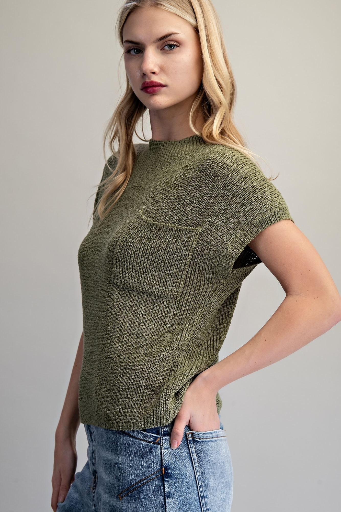 Woman wearing a green knitted top with a pocket against a gray background