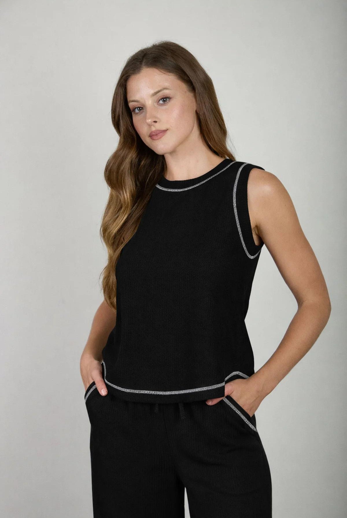 Woman wearing a black sleeveless top and pants with white trim on a gray background