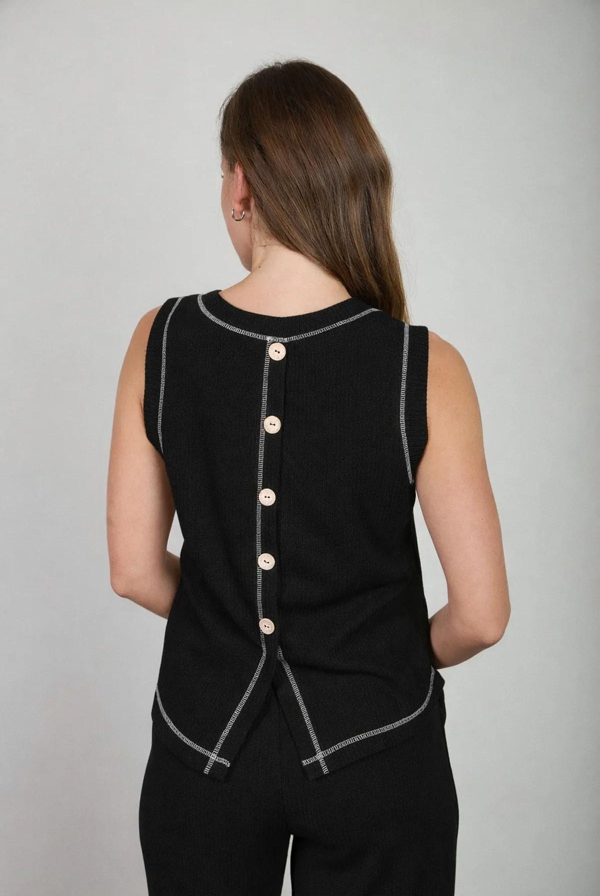 Woman wearing a black sleeveless top with button details on a gray background