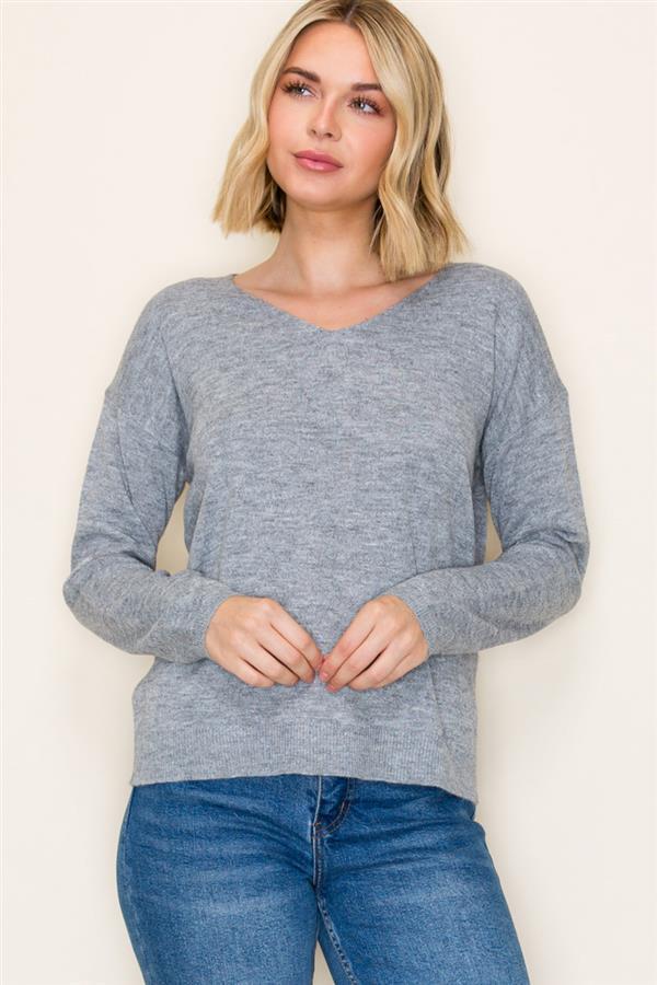 Woman wearing a gray sweater and blue jeans against a plain background