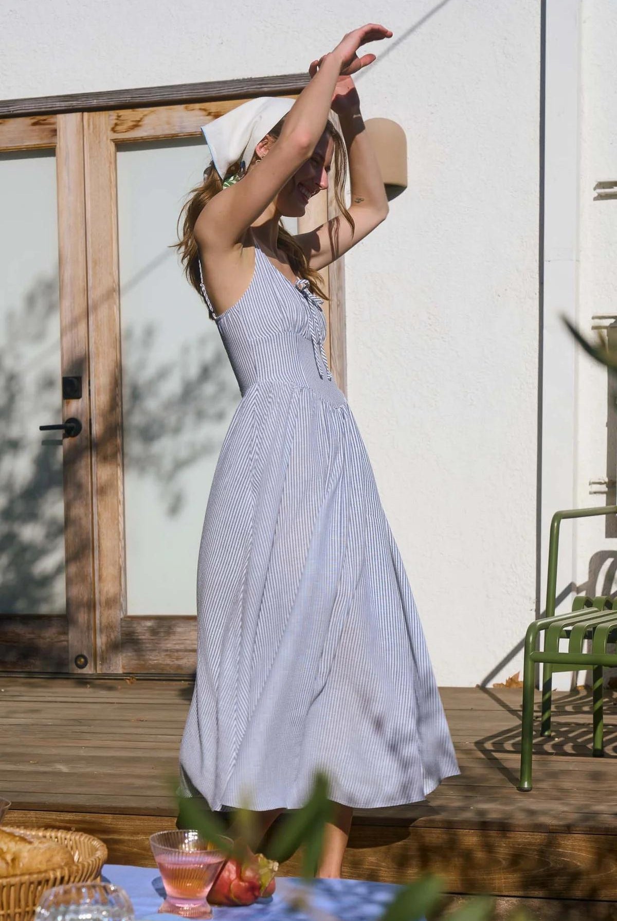 Woman in a light blue dress standing outdoors on a wooden deck.