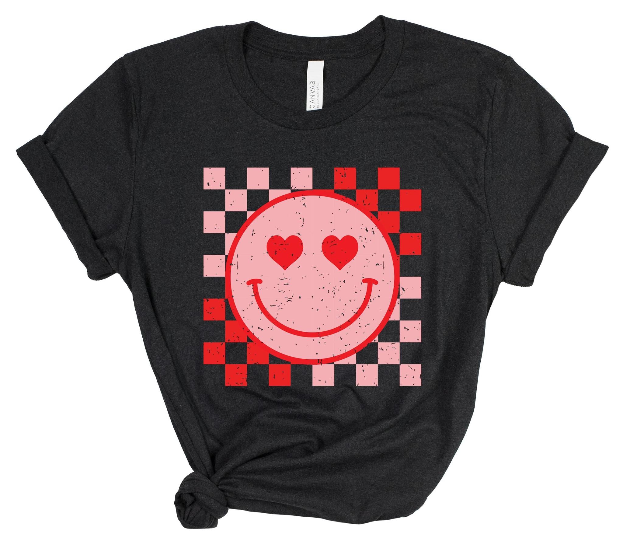 Black t-shirt with a pink smiley face with heart eyes on a checkered background