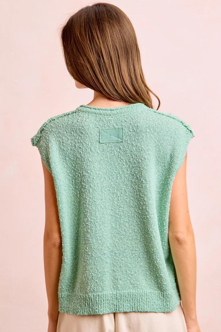 Woman wearing a light green sleeveless top against a pink background
