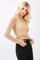 Woman wearing a beige long-sleeve top and black pants on a white background