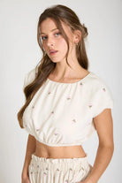 Woman wearing a white top with small patterns on a plain background