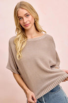 Woman wearing a beige knit poncho against a pink background