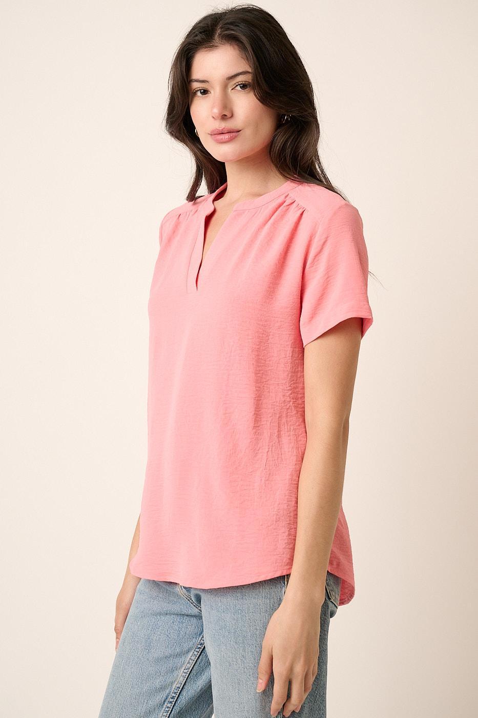 Woman wearing a pink blouse with short sleeves against a beige background