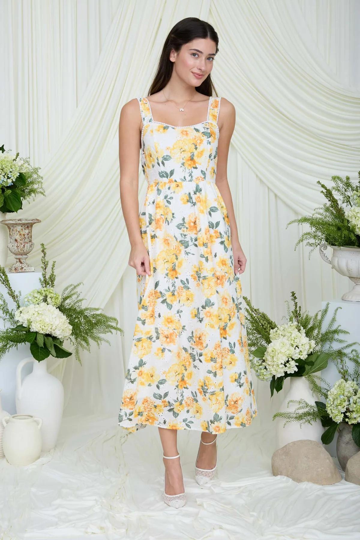 Woman wearing a yellow floral dress standing in a decorated room with white drapes and floral arrangements.
