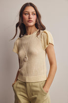 Woman wearing a beige knitted top and light green pants against a neutral background