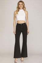 Woman wearing a white sleeveless top and black flared jeans on a plain background