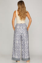 Woman wearing a sleeveless top and patterned pants on a plain background