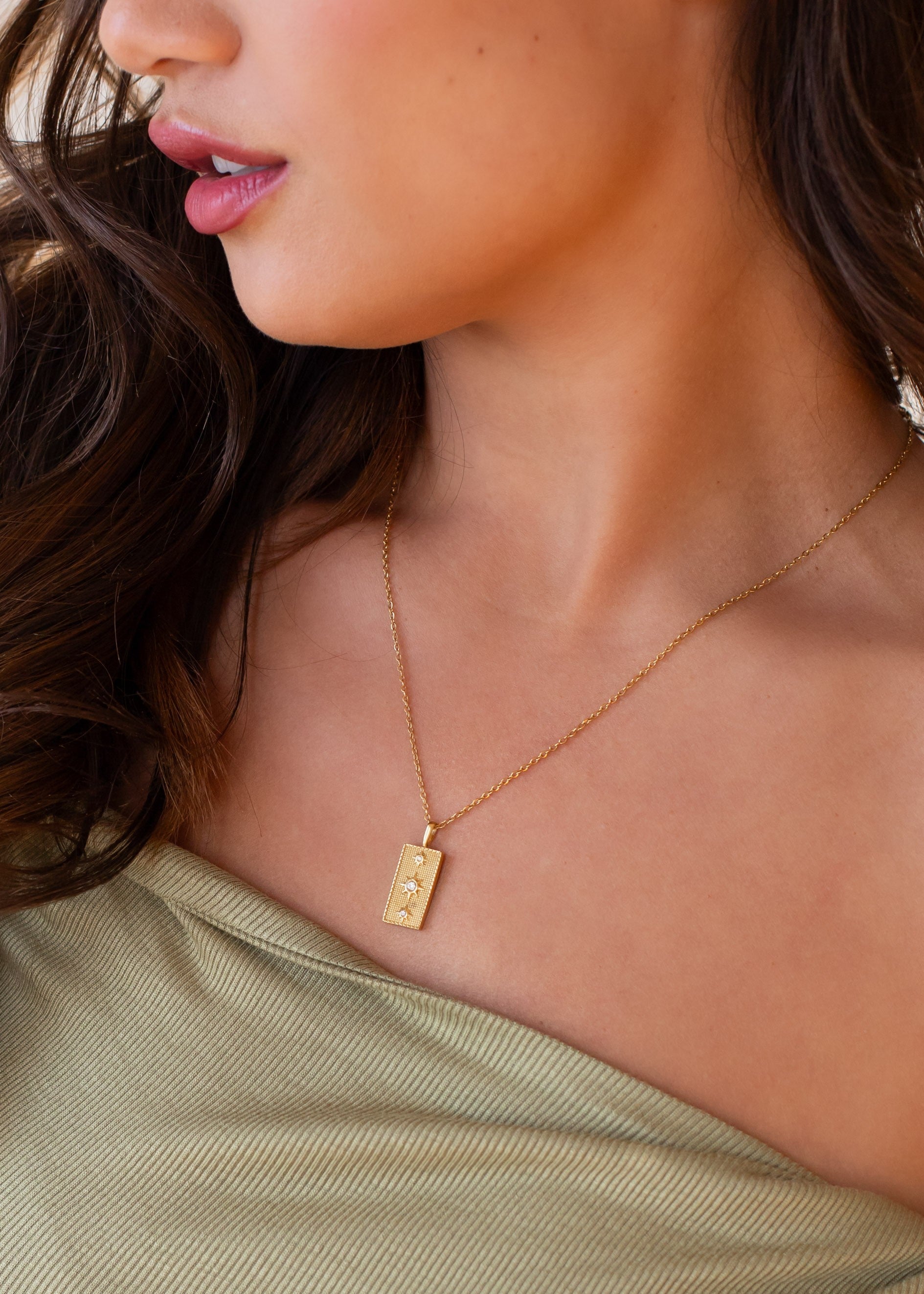 Close-up of a person wearing a gold necklace with a pendant.
