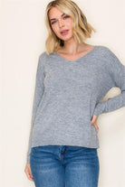 Woman wearing a gray sweater and blue jeans against a plain background