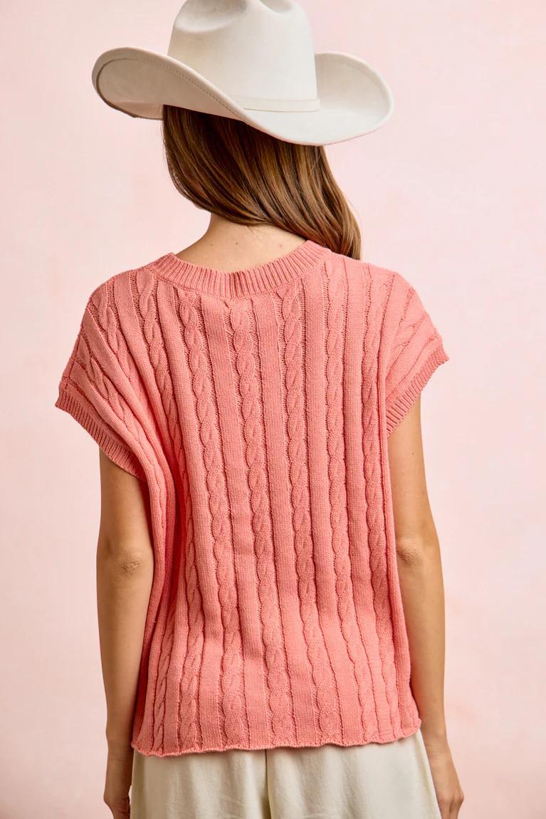 Person wearing a pink knitted top and white hat on a pink background