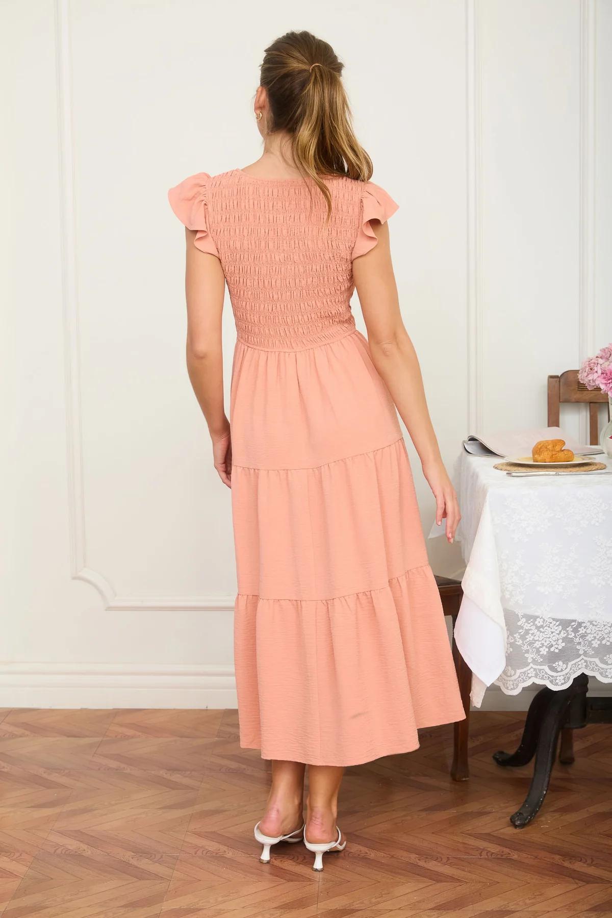Woman in a peach dress standing in a room with wooden flooring and a table in the background.