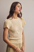 Woman wearing a light yellow knit top with short sleeves against a neutral background