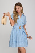 Woman wearing a blue striped dress holding a beige handbag on a gray background