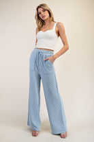 Woman wearing a white top and light blue wide-leg pants on a beige background