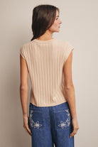 Woman wearing a beige ribbed top and blue jeans with floral embroidery on a beige background