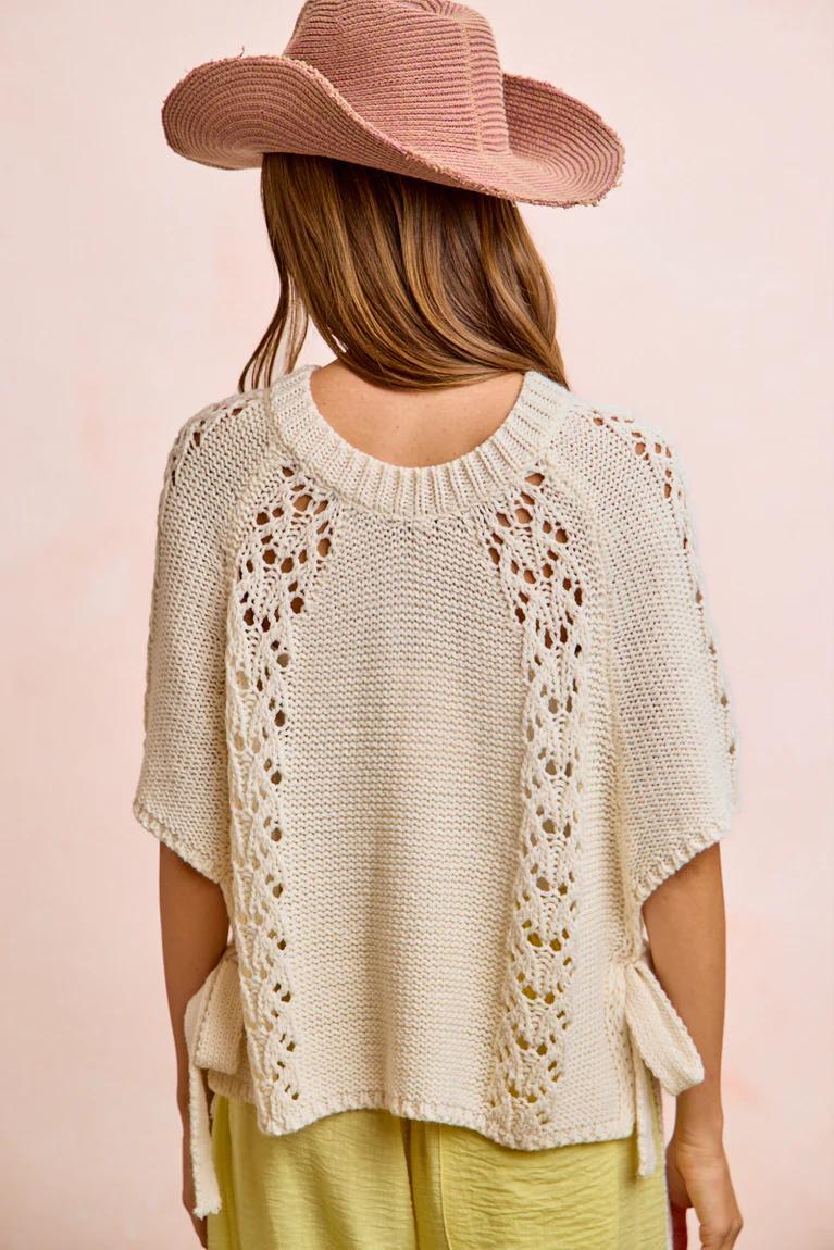 Woman wearing a beige knitted poncho with floral patterns on a pink background