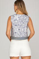 Woman wearing a sleeveless patterned top and white shorts on a plain background
