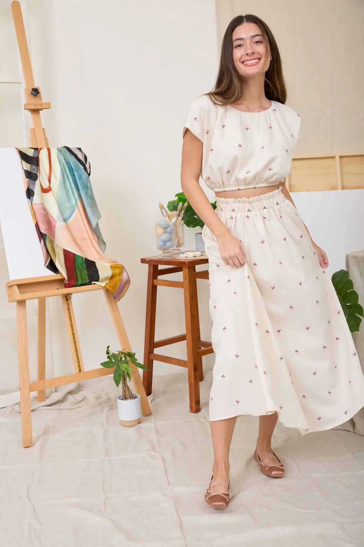 Woman in a white dress standing in an artist's studio with art supplies.