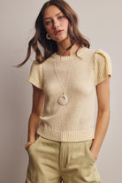 Woman wearing a light yellow knit top with puffed sleeves and beige pants against a neutral background