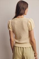 Woman wearing a beige knitted top with short sleeves against a plain background