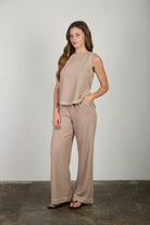 Woman wearing a beige sleeveless top and pants against a plain background