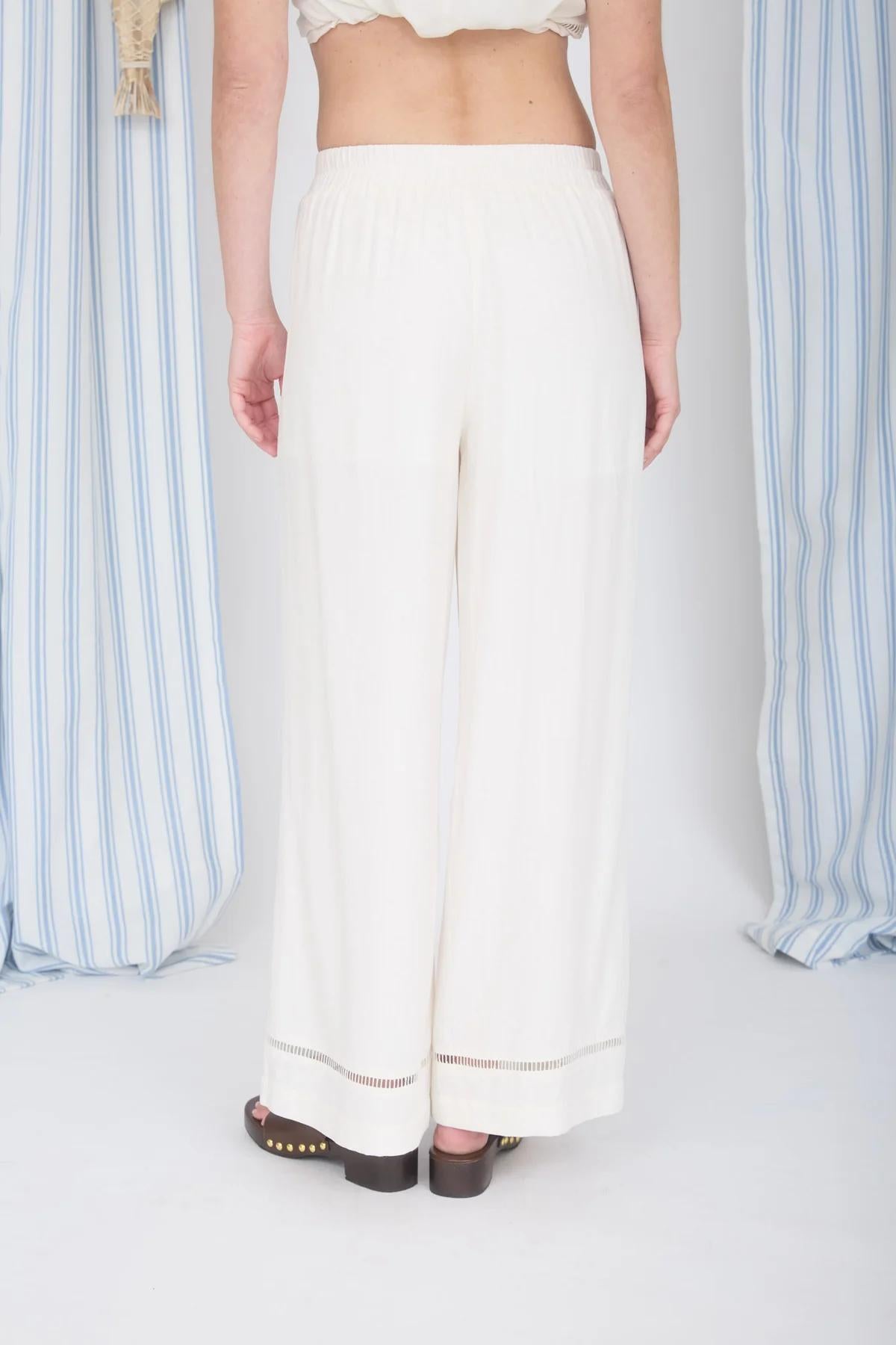 Person wearing a white outfit with wide-leg pants against a striped curtain background