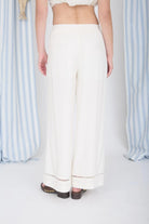 Person wearing a white outfit with wide-leg pants against a striped curtain background