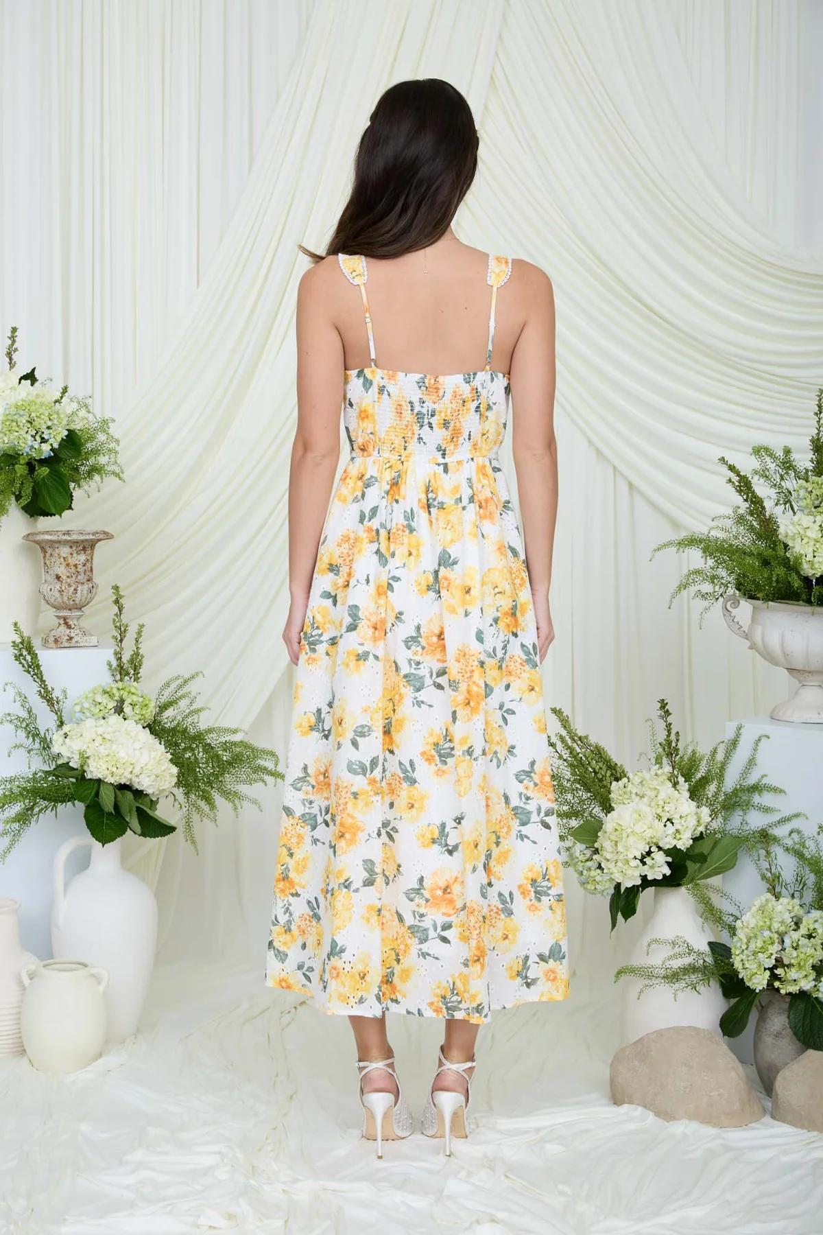Woman wearing a floral dress standing in front of a white draped backdrop with floral arrangements.