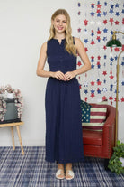 Woman in a navy dress standing in a room with a decorative wall and furniture.