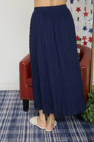 Person wearing a navy blue skirt standing in front of a red chair with star-patterned wallpaper.